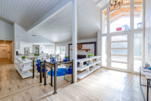 Modern and welcoming rehab facility common area featuring vaulted ceilings, large windows, lounge seating, and open shelving.