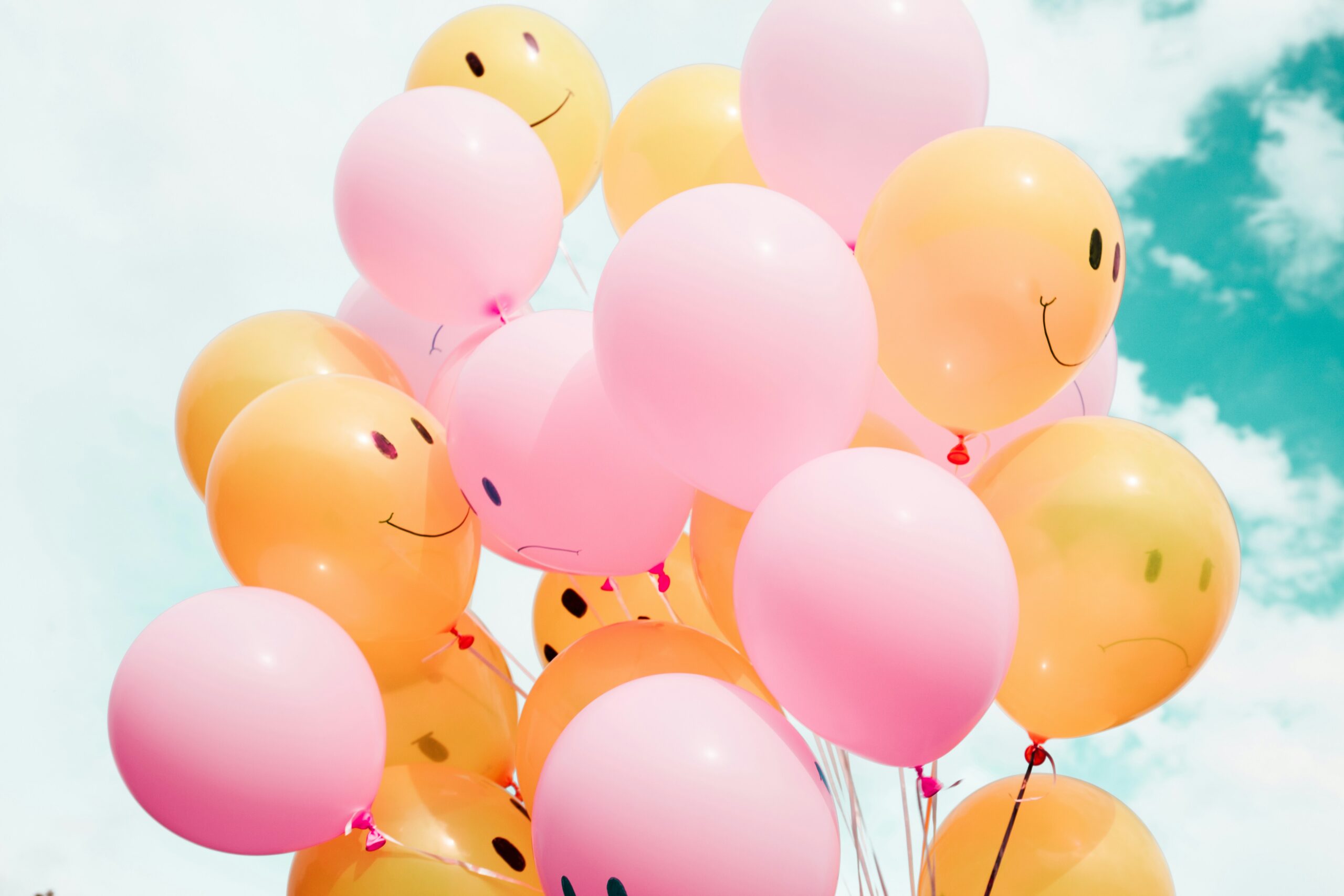 Blue and Pink smiley face balloons floating up together to the sky