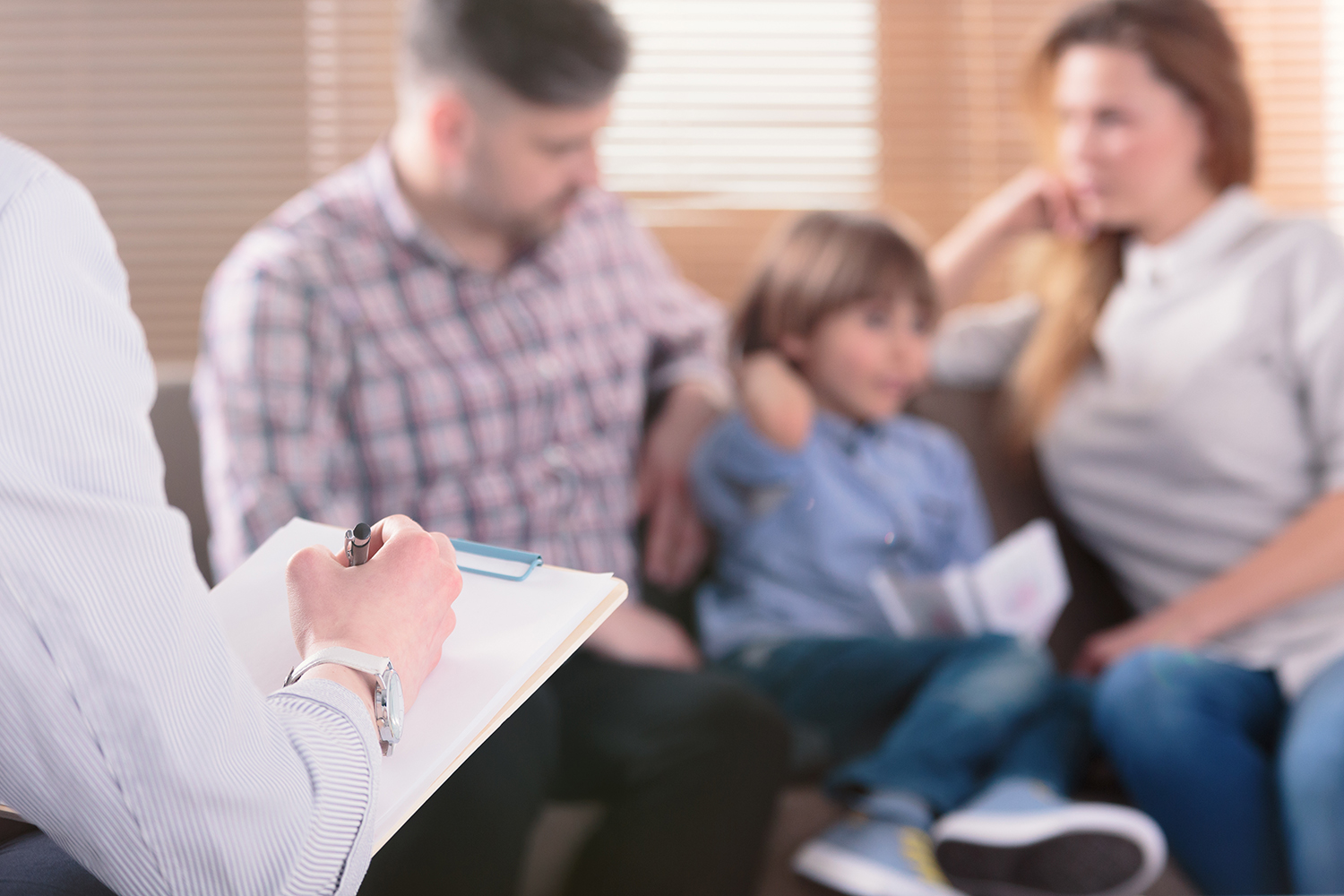 Therapist taking notes during a family counseling session with a couple and child in a recovery center.