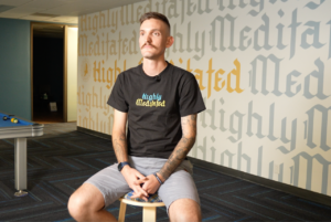 Man sitting calmly in a wellness center wearing a 'Highly Meditated' t-shirt, reflecting a peaceful post-therapy moment.