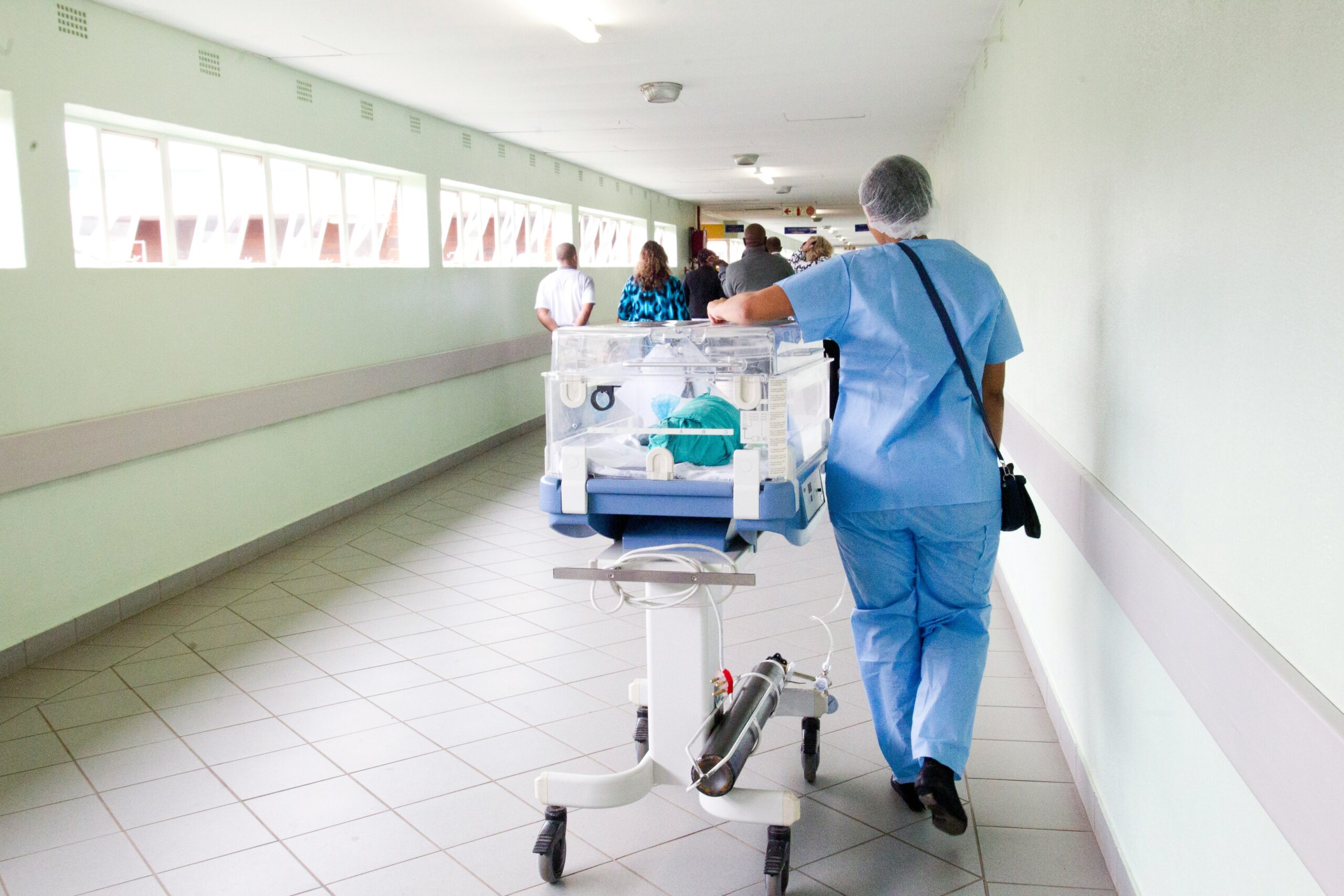 Nurse in blue scrubs walking through a hospital hallway while transporting an incubator at Saint Agnes Medical Center.