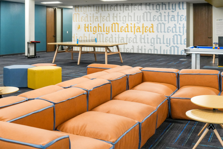 Modern outpatient treatment lounge with modular orange seating, round tables, and a wall featuring the phrase 'Highly Meditated.