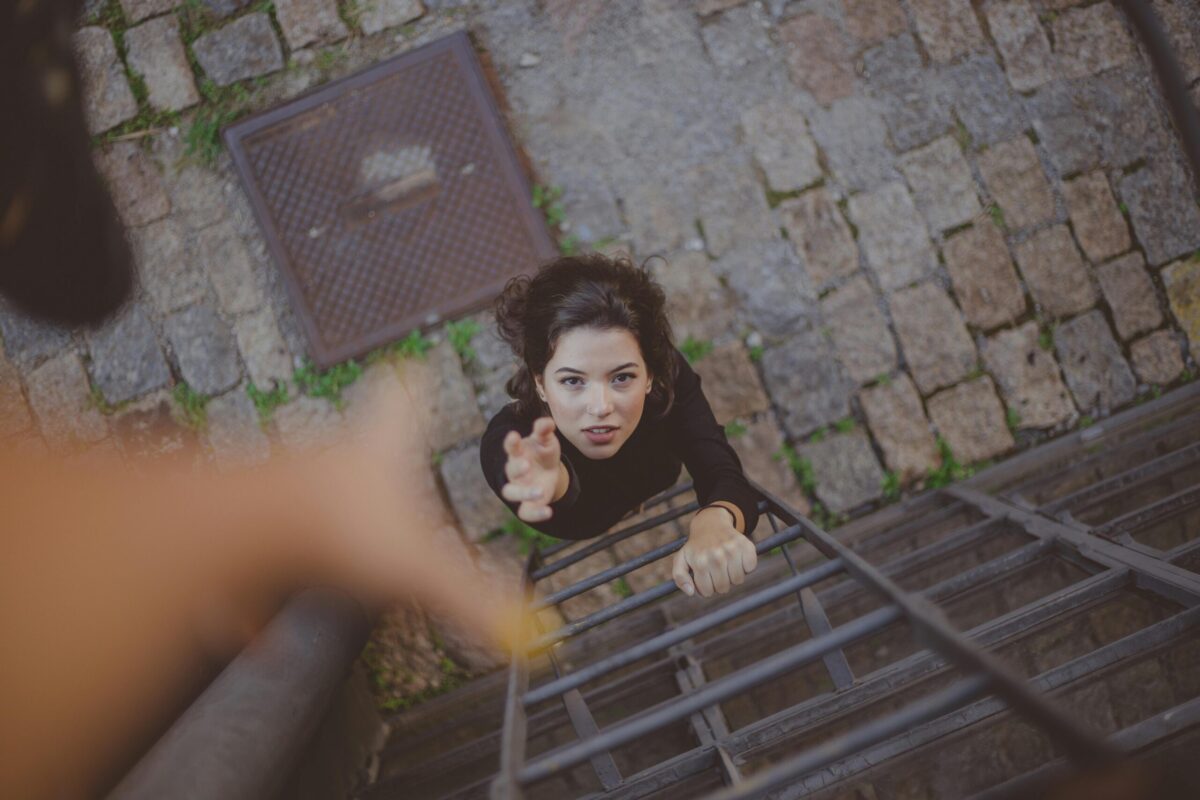 Woman reaching for help while climbing a ladder, symbolizing addiction recovery support.
