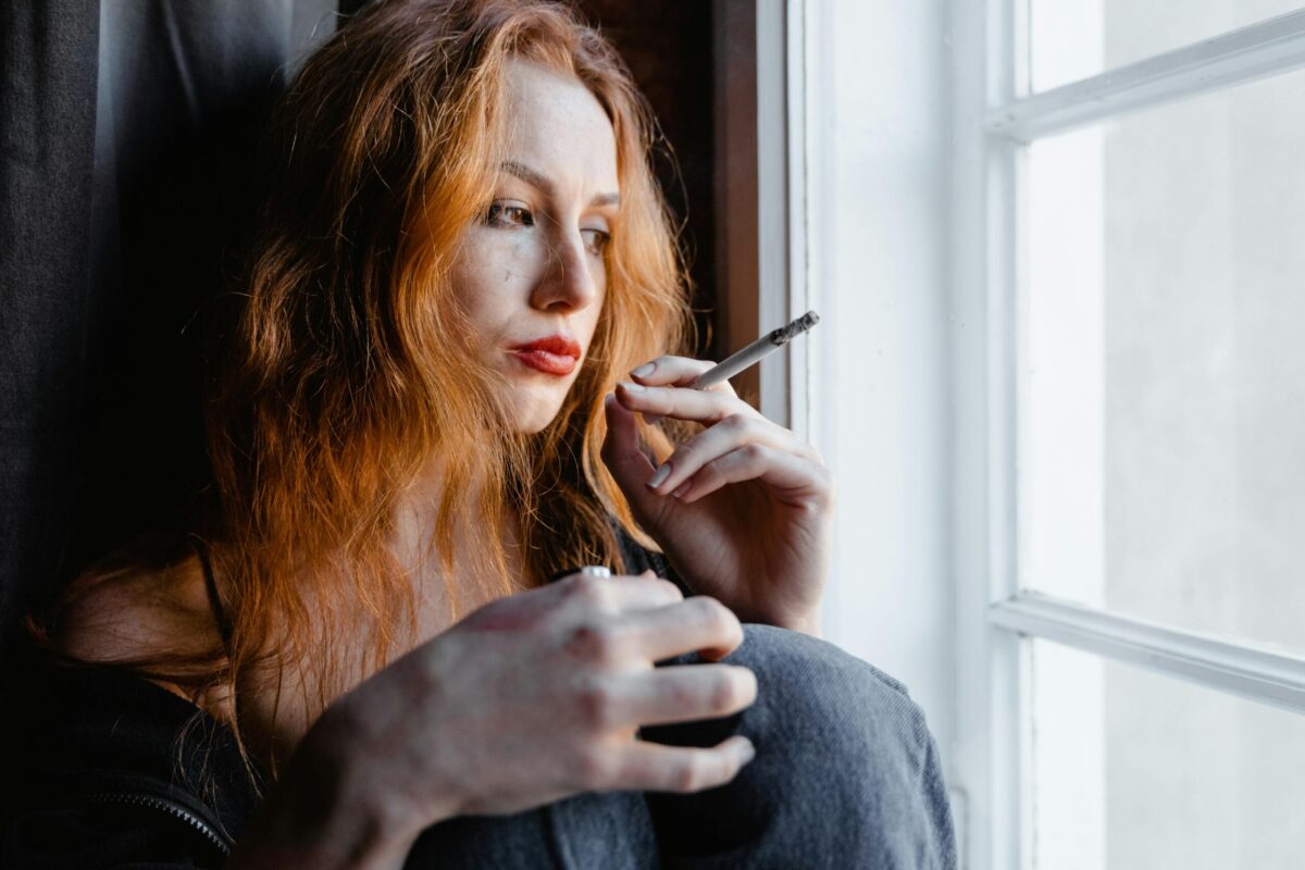 Close up of a woman sitting by a window smoking.