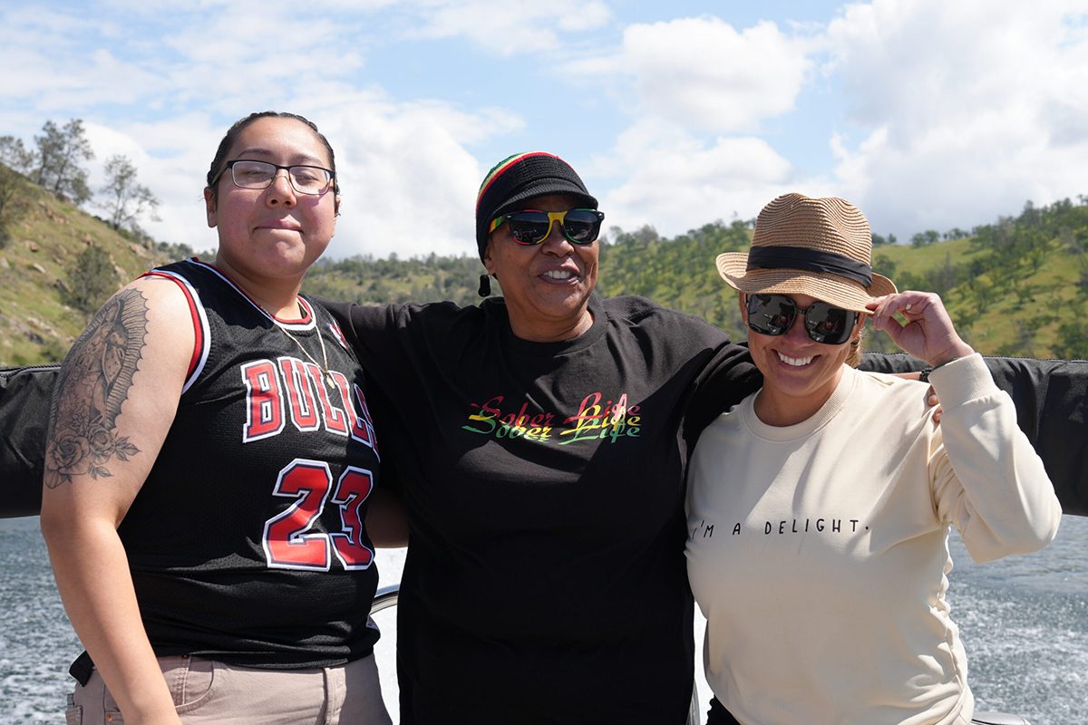 Three women smiling outdoors during a sober living adventure and recovery outing.